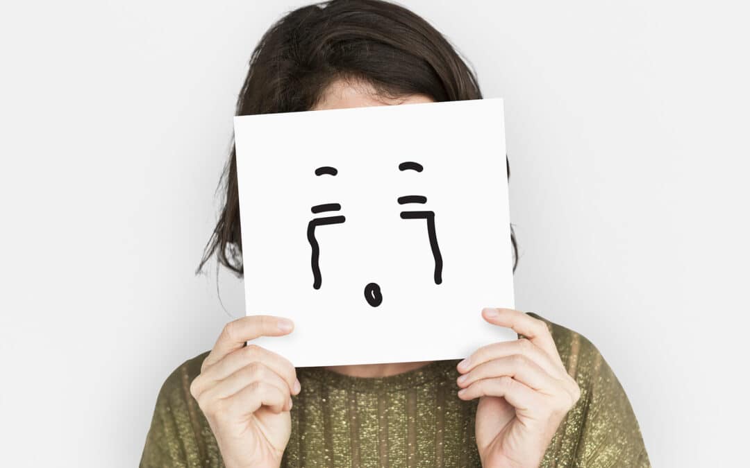 A woman holding up an illustration of a crying face in front of her own face