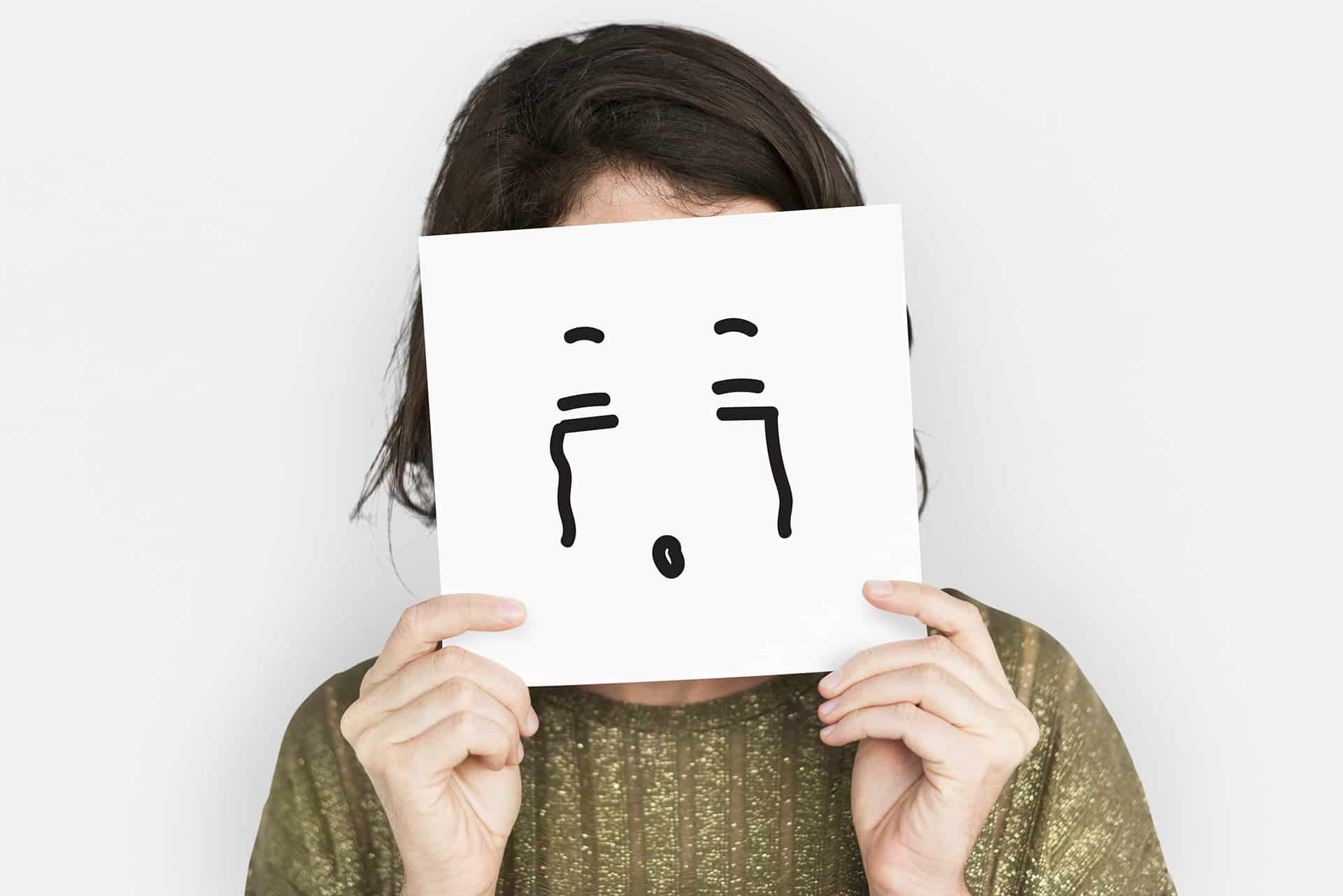 A woman holding up an illustration of a crying face in front of her own face