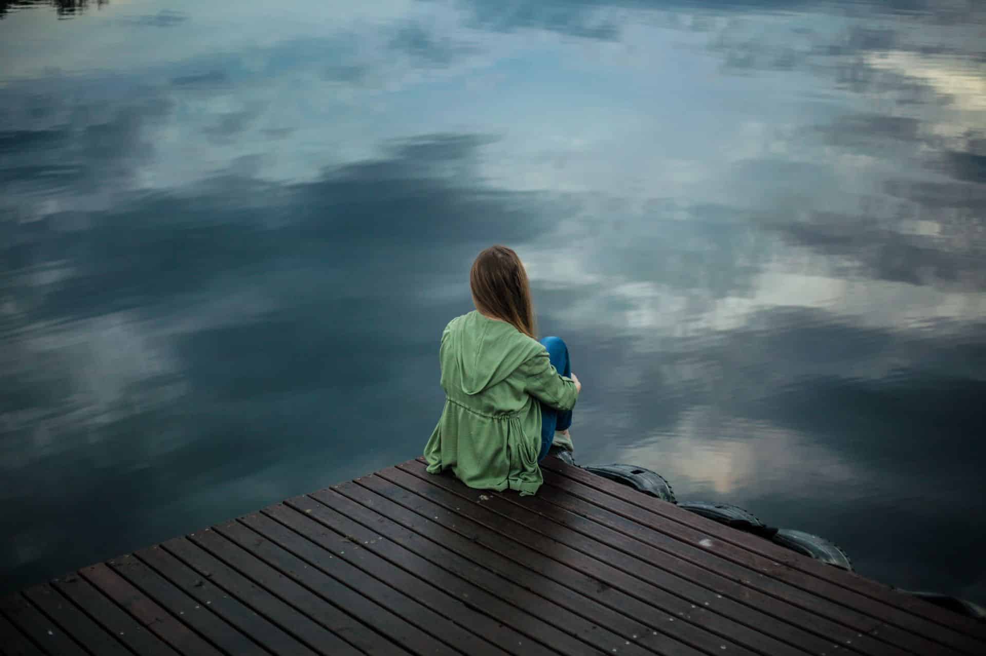 A woman sitting peacefully by the water, reflecting on life and symbolizing emotional resilience and inner strength.